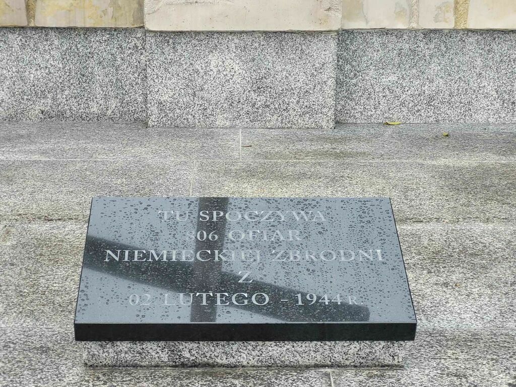 
                                                    Kamienna tablica upamiętniająca ofiary zbrodni w Borowie, z napisem w języku polskim, mokra od deszczu.
                                                