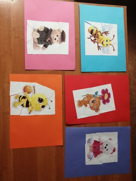 
                                                     Na zdjęciu znajdują się ułożone na stole kolorowe obrazki wykonane przez dzieci. Są to ułożone i przyklejone do kolorowych kartek puzzle. Trzy obrazki przedstawiają misie, a dwa pszczółki.
                                                