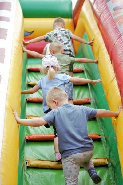 Na zdjęciu widać czworo dzieci wchodzących na dmuchańca. Dzieci są tyłem. Wchodząc do góry ręce mają zaparte o boki dmuchańca. 