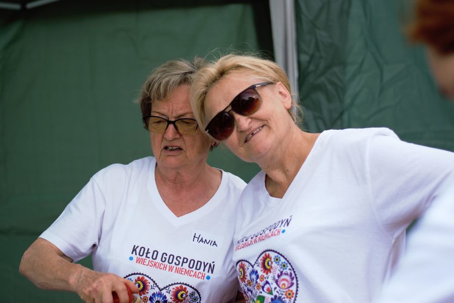 Zdjęcie przedstawia dwie uśmiechnięte kobiety, jedna ma okulary, obie mają białe koszulki z logo Koła Gospodyń Wiejskich w Niemcach