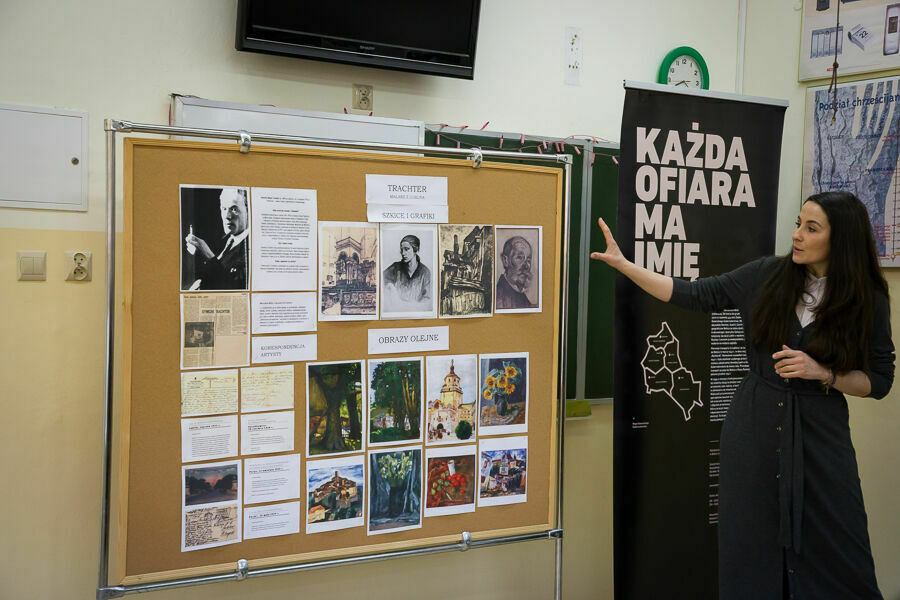 Kobieta prezentuje prace plastyczne uczniów o holokauście