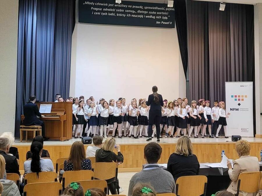 na scenie duża grupa dzieci ubrana na biało-czarno