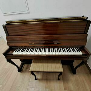 Stary brązowy fortepian z drewna z otwartą klapą i stołkiem na podłodze z paneli.