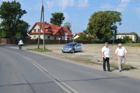 
                                                    3 osoby przy ulicy na tle domków
                                                