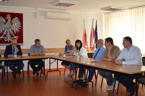 
                                                    Grupa siedzących ludzi na tle godła
                                                