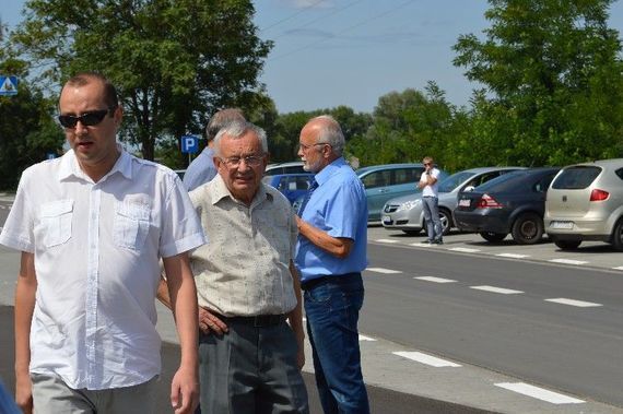 
                                                    Grupa osób stojących na chodniku na tle samochodów
                                                