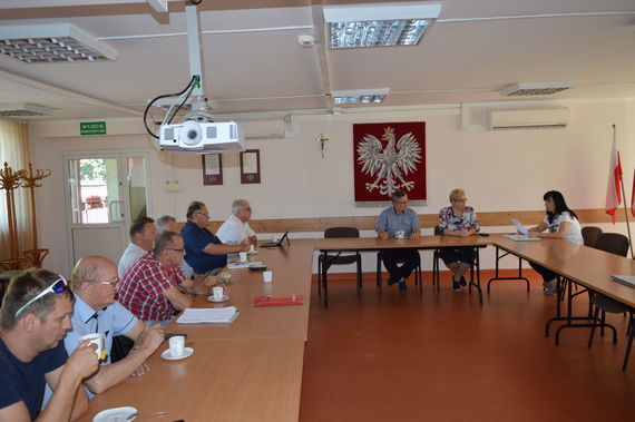
                                                    Grupa siedzących ludzi na tle godła
                                                