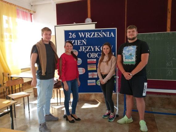 
                                                    cztery osoby przy tablicy promującej  dzień języków obcych
                                                