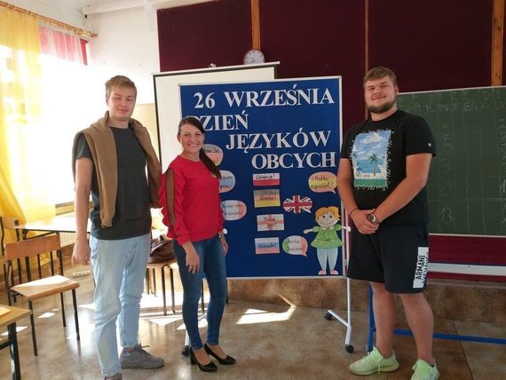 
                                                    Trzy osoby przy tablicy promującej dzień języków obcych
                                                