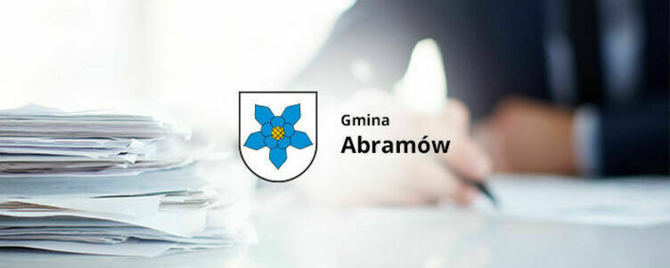 Na zdjęciu widoczne jest biuro z pracującą osobą oraz stosem papierów, z logo "Gmina Abramów" w centralnym punkcie.