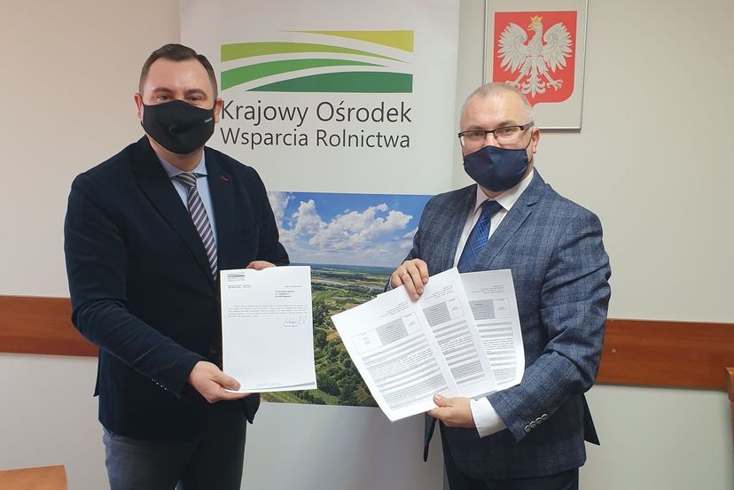 Na zdjęciu widnieją: Pan Marek Wojciechowski - Zastępca Dyrektora Krajowego Ośrodka Wsparcia Rolnictwa oddział w Lublinie oraz Pan Ireneusz Łucka Burmistrz Bełżyc. W tle widnieje logo Krajowego Ośrodka Wsparcia Rolnictwa oraz godło Polski. Zdjęcie wykonane w związku z pozytywną opinią dyrektora KOWR w Lublinie dotyczącą wsparcia gmin popegeerowskich z Rządowego Funduszu Inwestycji Lokalnych to środki przeznaczone na sfinansowanie lub dofinansowanie inwestycji i zakupów inwestycyjnych w gminach, w których funkcjonowały niegdyś zlikwidowane państwowe przedsiębiorstwa gospodarki rolnej, w wysokości od 50 tys. zł do 5 mln zł.