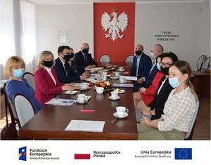Zdjęcie przestawia osoby siedzące przy stole. U dołu zdjęcia znajdują się loga: Od lewej strony logo Funduszy Europejskich, po środku znajduje się Flaga Polski i napis Rzeczpospolita Polska, po prawej stronie znajduje się flaga Unii Europejskiej i napis Unia Europejska Europejski Fundusz Społeczny. 