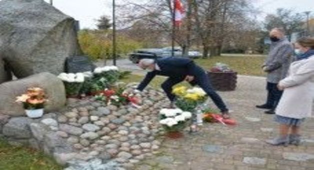 Ludzie w maseczkach składający kwiaty przy pomniku