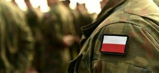 Grupa ludzi w mundurach wojskowych, widać ramiona z naszywką flagi Polski na jednym z nich, niewyraźne tło.