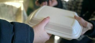 Osoba przekazuje innemu człowiekowi styropianowe pudełko na jedzenie. Widzimy tylko ręce i pudełko.