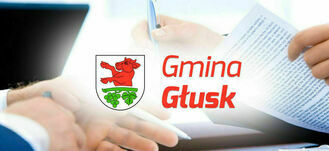 Osoba w garniturze podpisuje dokument; w tle widoczne są logotypy: herb z czerwonym bykiem oraz napis "Gmina Głusk".