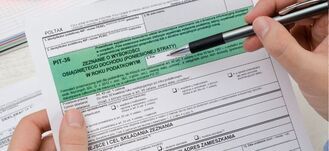 Ręka trzymająca długopis nad wypełnionym formularzem PIT-36 dotyczącym rocznego zeznania podatkowego w Polsce.