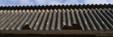 Opis alternatywny: Starzejący się azbestowo-cementowy dach faliści o fakturze szarej z wyraźnymi zielonymi porostami.