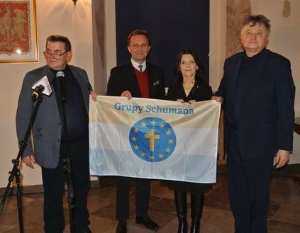 Cztery osoby trzymają flagę z logo Grupy szumana