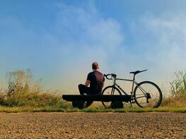 mężczyzna siedzący na ławce, obok stoi rower 