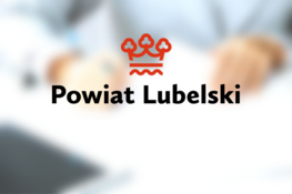 Logo Powiatu Lubelskiego z trzema koronami na tle rozmytych postaci ludzkich i sprzętu biurowego, sugerujące oficjalne lub administracyjne użycie.