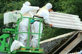 Pracownicy w białych kombinezonach ochronnych usuwają azbestowe płyty z dachu, używając podnośnika koszowego. Zdjęcie pobrane ze strony https://www.gov.pl/web/arimr/kpo-dofinansowanie-wymiany-dachow-z-azbestu--nabor-startuje-15-grudnia