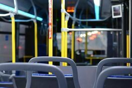 Wnętrze pustego autobusu nocą z niebieskimi siedzeniami i żółtymi uchwytami. Widok z perspektywy pasażyera siedzącego z tyłu.