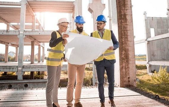 Trzech architektów w kaskach przy planie na tle budowy