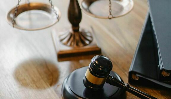 Drewniany młotek sędziowski i waga sprawiedliwości na biurku z laptopem w tle, symbolizujące prawo i sądownictwo.