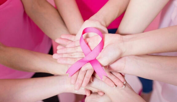 Ręce układające się wokół różowej wstążki symbolizującej wsparcie dla osób z rakiem piersi, położone na stole.