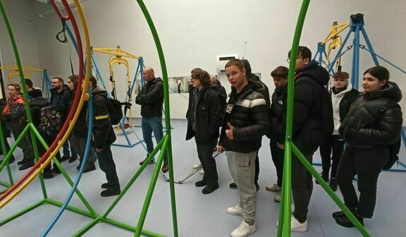 Grupa ludzi ogląda i korzysta z interaktywnych, kolorowych rzeźb w nowoczesnej galerii sztuki.