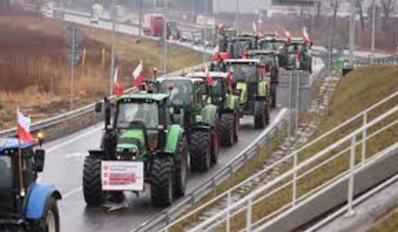 Protest rolników z udziałem ciągników na autostradzie; widoczne flagi i transparenty, mokra droga, ponure niebo.