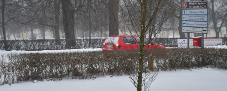 Zamieć śnieżna na ulicy, w tle czerwone auto i znaki miejskiego systemu informacji