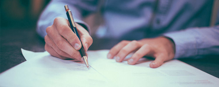 Zdjęcie przedstawia ręce składające podpis na dokumentach.