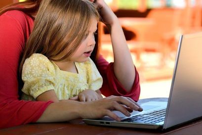 Dziewczynka siedząca na kolanach u mamy przed laptopem