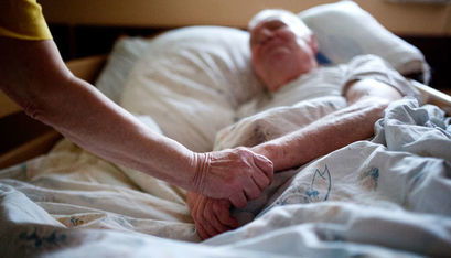 Pacjent leżący na łóżku i trzymająca jego dłoń osoba