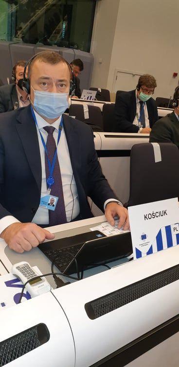 Burmistrz Krasnegostawu Robert Kościuk siedzi  w słuchawkach przy biurku na spotkaniu w Brukseli, na biurku leży laptop