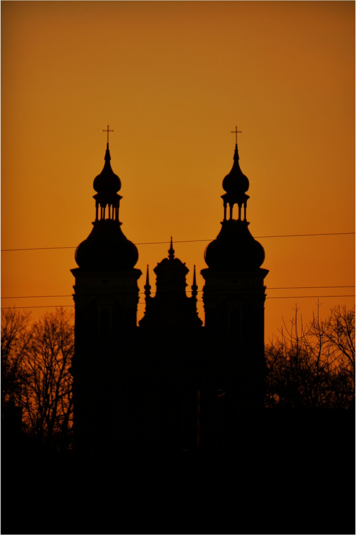 Zarys wież kościoła na tle pomarańczowego nieba o zachodzie słońca.